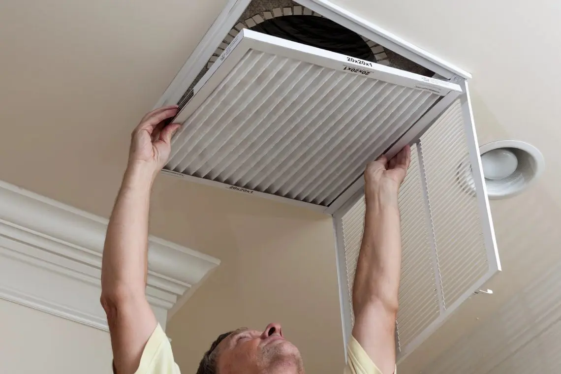 A man is holding an air filter up to the ceiling.